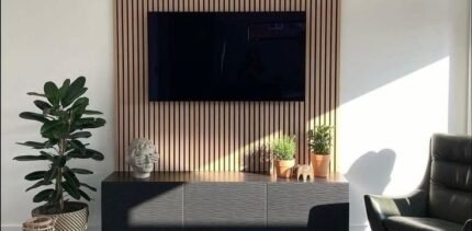 Modern slatted wood panel TV wall with a floating cabinet and potted plants.