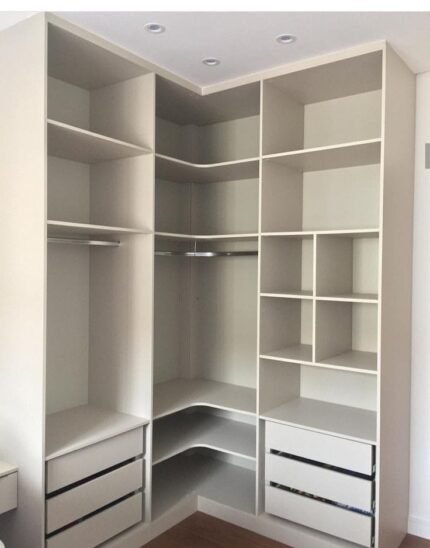 Functional white walk-in closet with corner shelving, hanging rods, and drawers.